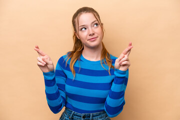 Young caucasian woman isolated on beige background with fingers crossing and wishing the best