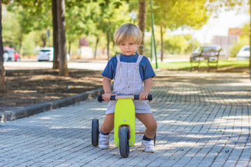 2 year old blond toddler playing and enjoying a sunny day in the park with his tricycle. Little boy...