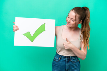 Young caucasian woman isolated on green background holding a placard with text Green check mark icon and  pointing it