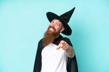 Young wizard in halloween isolated on blue background pointing front with happy expression