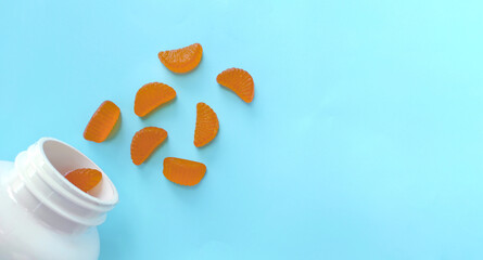 Blue background with vitamin C gummies in the form of orange slices. Space for text