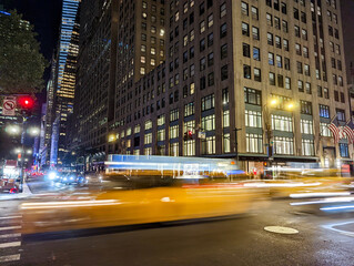 Blurred motion of a yellow taxis driving down the street through New York City at night with...