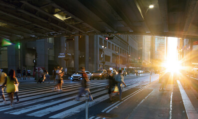 Sunlight shining on people walking across a busy street crosswalk at Grand Central Station in...