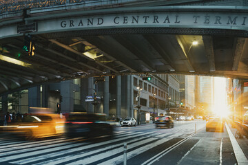 Taxis and cars driving down a busy street past Grand Central Station in New York City with sunlight...