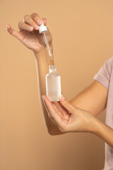 female hands holding bottle and pipette on beige background