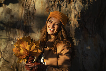 happy woman in beige coat and orange hat against huge tree