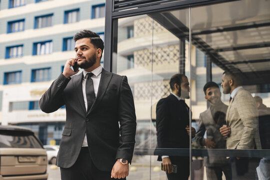Portrait of a business man outdoors using the phone against the backdrop of a glass building downtown.