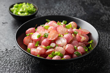 Roasted radish with spring onion and herbs in a black bowl