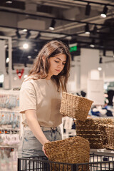 A young woman chooses baskets for a home interior in a home improvement store.