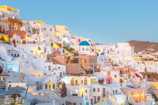Seaside view at blue hour of traditional white wash buildings and blue dome churches at the popular seaside tourist resort village of Oia on the Greek island of Santorini, Greece. © Stephen
