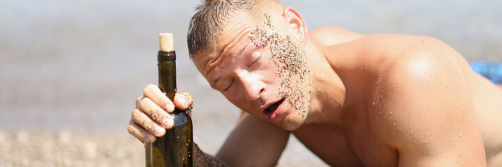 Drunk man with bottle of wine lies on beach