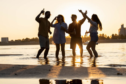 Silhouette of friends on beach dancing in the water