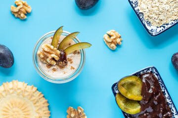 Dessert mit Pflaume, Walnuss, Frischkäse, Joghurt. Quark, Haferflocken, Marmelade und Zimt auf einem Tisch angerichtet