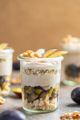 Dessert mit Pflaume, Walnuss, Frischkäse, Joghurt. Quark, Haferflocken, Marmelade und Zimt auf einem Tisch angerichtet