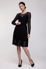 High fashion photo of a beautiful elegant young woman in a pretty black long dress with sleeves posing over white, soft gray background. Studio Shot. 