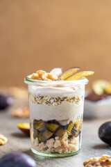 Dessert mit Pflaume, Walnuss, Frischkäse, Joghurt. Quark, Haferflocken, Marmelade und Zimt auf einem Tisch angerichtet