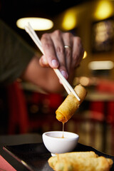 Fototapeta na wymiar Rollito de primavera mojado en salsa agridulce. Hombre comiendo en restaurante chino con palillos.