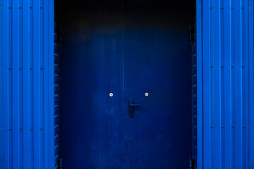 Blue metal wall. A blue metal door and a blue trash can next to it. background picture.
