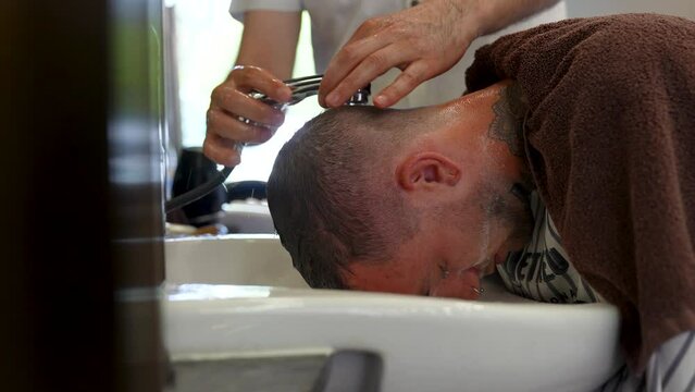 close up reveal of young Caucasian man getting his hair cut and washed in a salon