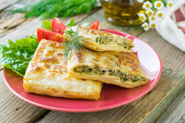 Fried pita bread stuffed with chicken, cheese and herbs served on a ceramic plate. Wooden background. Selective focus