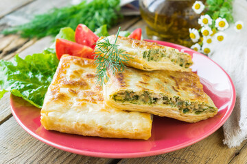 Fried pita bread stuffed with chicken, cheese and herbs served on a ceramic plate. Wooden...