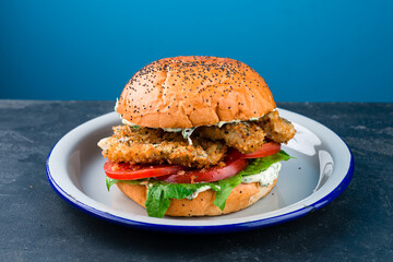 Fish burger on gray plate, blue background, copy space. Cod fish in batter with mayonnaise and spinach sandwich.