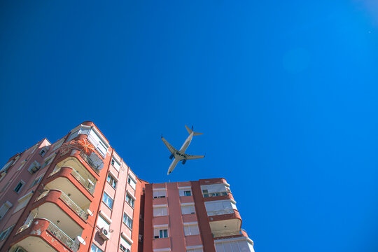 A passenger plane flies over a residential building against a background of blue sky and sun.