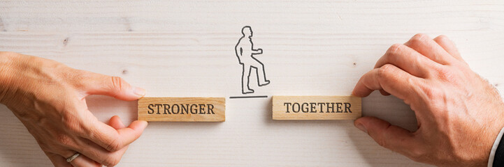 Hands of a businessman and businesswoman holding two wooden pegs with a Stronger together sign