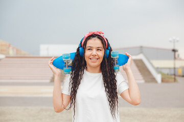 a young woman with dreadlocks holds a skateboard and listens to music.generation z