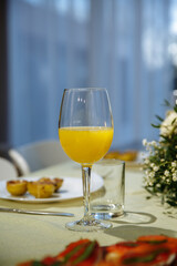 Glasses with yellow juice on the table, with flowers in the room