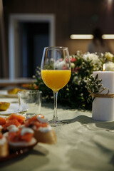 Glasses with yellow juice on the table, with flowers in the room