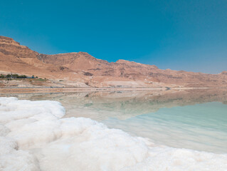 Fototapeta na wymiar Landscape view on Dead Sea salt crystals formations, clear cyan green water and mountains at Ein Bokek beach, Israel