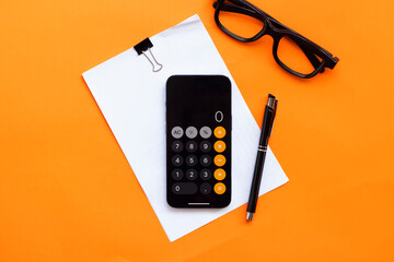 Calculator, a pen, a notebookand eye glasses on orange background. Finance, tax, accounting,...