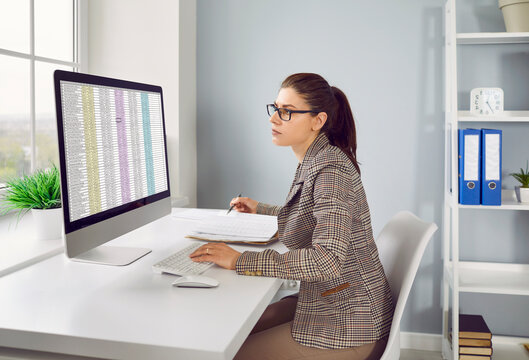 Accounting. Concentrated female financier calculates company's internal accounts using Excel spreadsheet. Woman checks financial documents and plans budget while sitting at her workplace in office.
