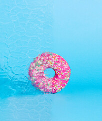 Minimal party concept donut with pink topping behind a glass window. Creative idea a delicacy on a blue background.