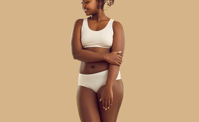 Young African American woman in underwear on yellow studio background pose in underwear. Smiling black ethnic girl in intimates feels body positive about natural curvy body figure or shape.