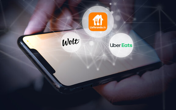 Logos der Lieferdienste f&uuml;r Essen Lieferando.de, Wolt und UberEats schweben &uuml;ber einem Smartphone und einem hellen Rasterlinien, Internet, Lieferservice, Lieferdienst, Gastronomie, Hunger, Ern&auml;hrung