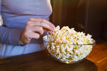 The girl reaches for the popcorn in a glass cup in the kitchen. Getting ready to watch a movie