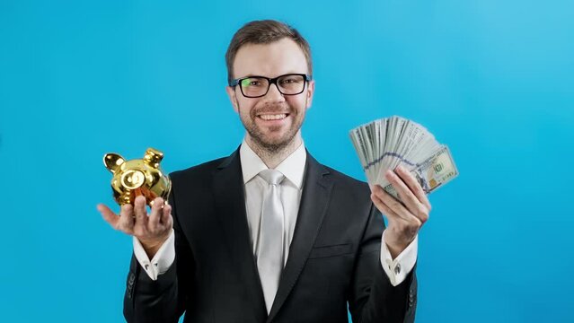 Happy businessman showing dollars and piggy bank over blue background. Concept of success and economy. Young bearded man. Investment and deposit concept.