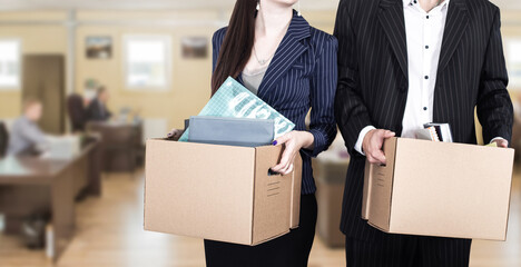 Man and woman are fired. Office workers need work. Fired mans box. Box with personal belongings symbolizes reduction of staff. Guy and girl in front of blurred office. Fired due to financial crisis - obrazy, fototapety, plakaty