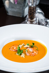 Delicious yellow pumpkin cream soup with shrimp on dark wooden table