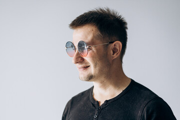 Fototapeta premium Handsome man in a black t-shirt and round glasses stands and looks confidently at the camera and smiles.