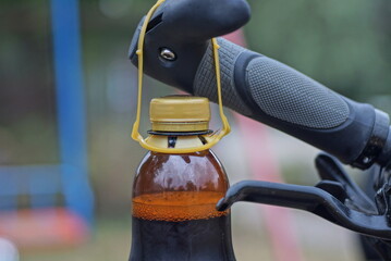 one brown plastic bottle with a drink hangs on a black handlebar of a bicycle in the street
