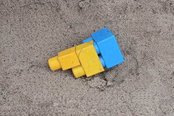 two yellow blue small plastic parts from a toy constructor lie on gray sand in the street