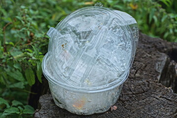 garbage from a pile of white plastic dishes stands on a gray wooden stump among green vegetation in nature