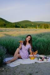 close-up portrait of a young beautiful woman in summer on a lavender field at a picnic with a basket of fruits, a baguette, a croissant