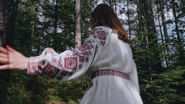 Back view of unrecognizable ukrainian woman walking in fir forest, Carpathian mountains nature. Girl in traditional embroidery vyshyvanka dress. Ukraine, freedom, ethnic national costume