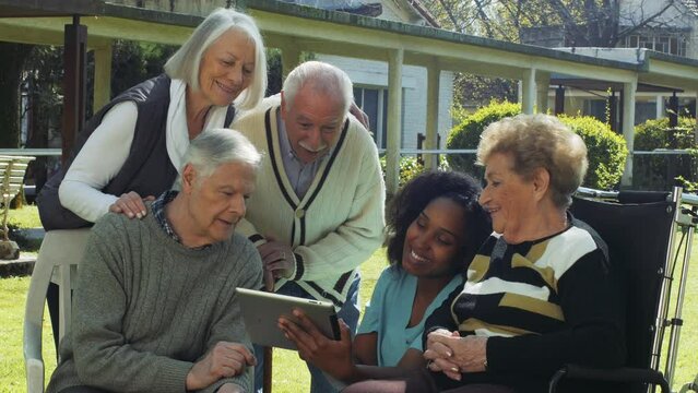 Group of elderly retired people in the garden smiling using tablet - Active seniors outdoor