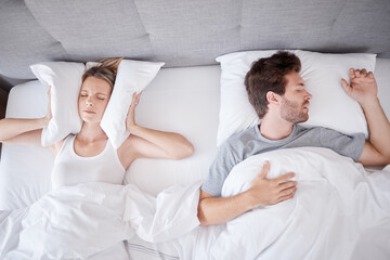 Sleeping, snoring and wife with pillow on ears to stop noise from husband in bed with sleep problem. Insomnia, frustration and stress with tired woman in bedroom lying next to man with apnea