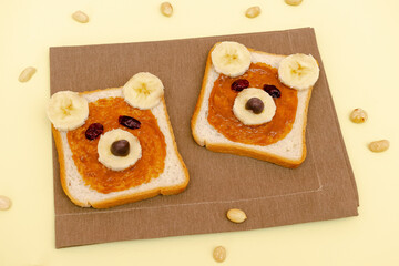 Funny cute bear faces sandwich toast bread with peanut butter, banana,nuts. Kids childrens baby's sweet dessert healthy breakfast lunch food art on plate,close up,top view